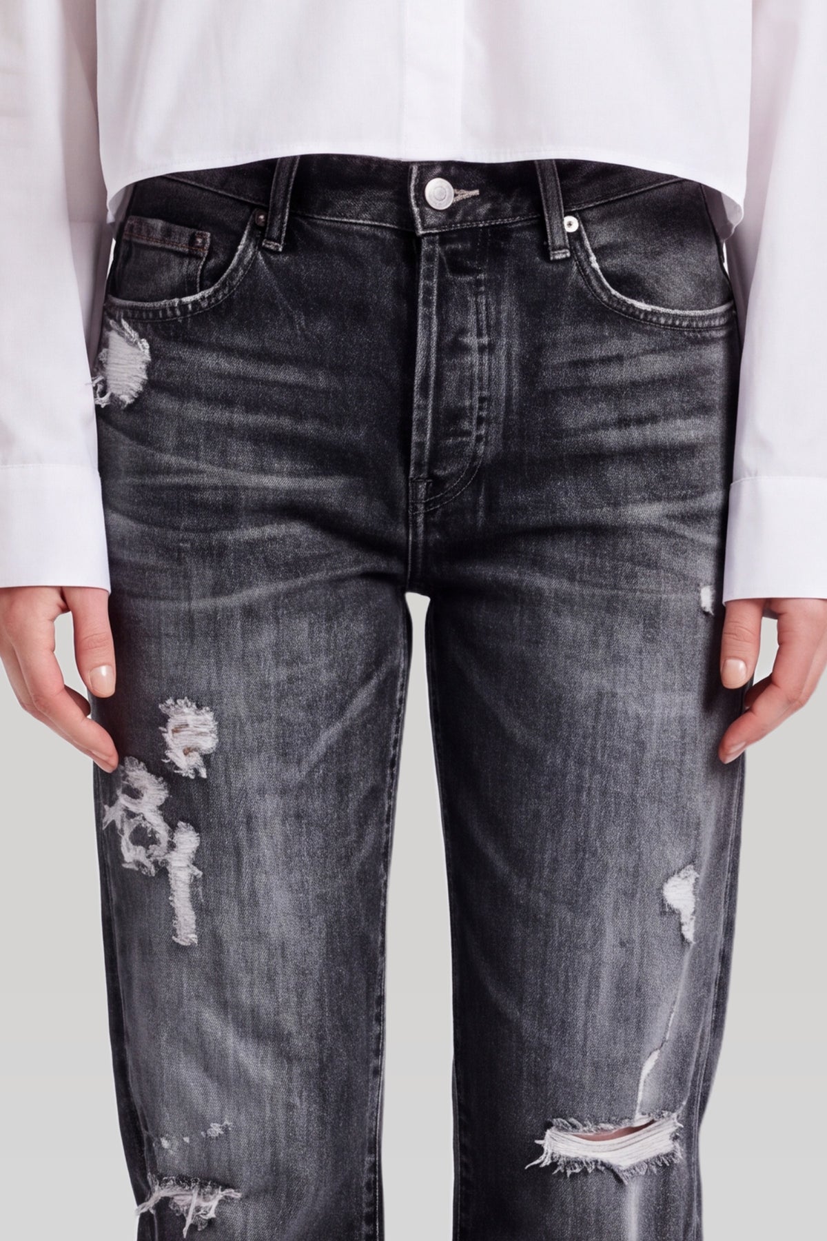 Nærbillede af sorte ripped jeans: knaplukning, lomme og revner