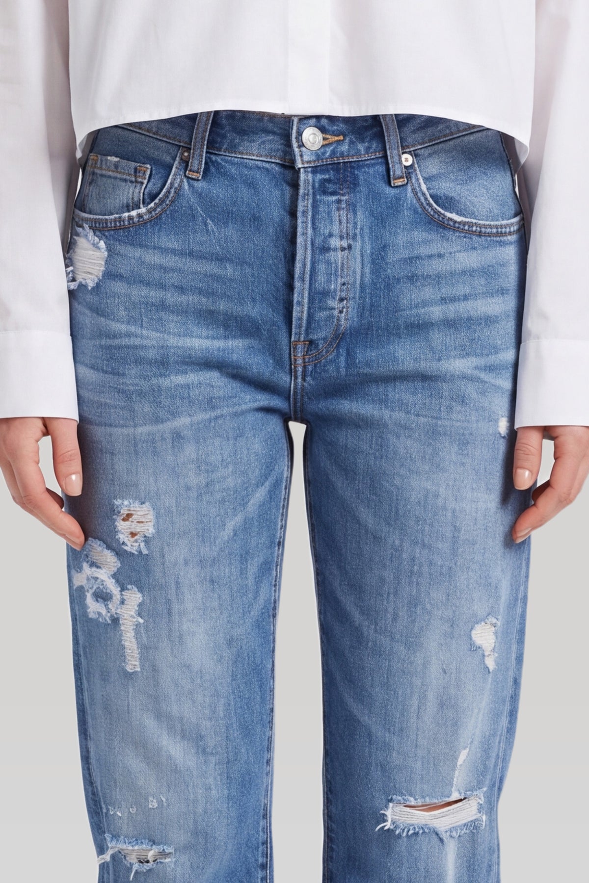 Nærbillede af blå ripped jeans: knaplukning, lomme og revner