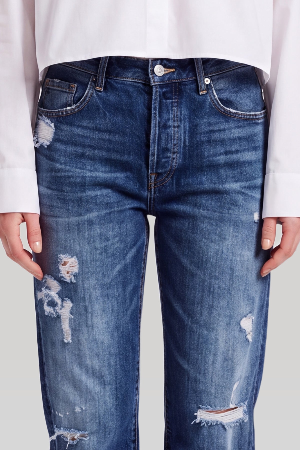 Nærbillede af mørkeblå ripped jeans: knaplukning, lomme og revner